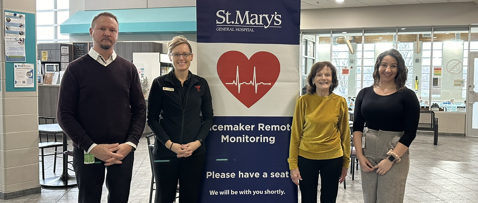 Four individuals stand side by side in front of a banner that has St. Mary's logo, an icon of a heart with a heartbeat and the words: Pacemaker Remote Monitoring. Please have a seat. We will be with you shortly.